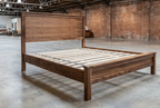 Walnut platform bed with panel headboard and exposed slats in an industrial interior scene