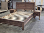 Side-angle workshop view of walnut platform bed and a two-drawer nightstand