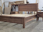 Angled view of walnut platform bed frame and nearby nightstand in the workshop